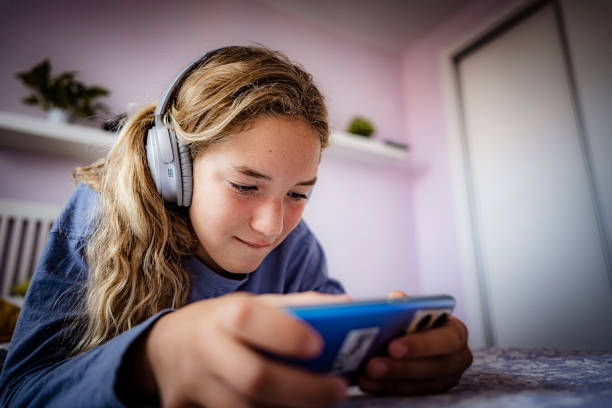 ragazza adolescente sdraiata sul letto che gioca a un videogioco con smartphone - one teenage girl only on the phone bed lying on front foto e immagini stock