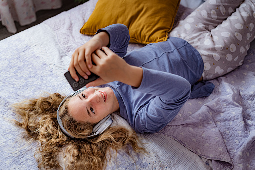 Relaxed teen girl listening music laying on her bedroom.