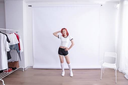 Redhead woman in a white shirt and black shorts posing in a studio,