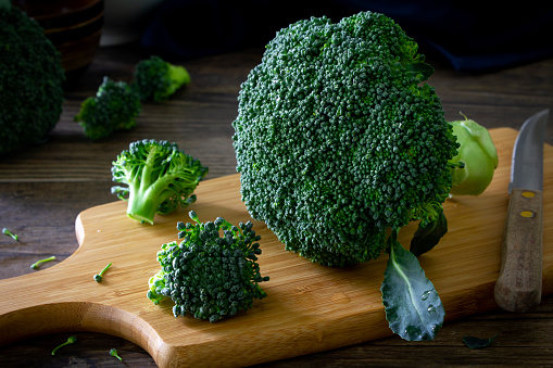 Close up shot of fresh broccoli and chopped broccoli on a chopping board, on a rustic wooden table.