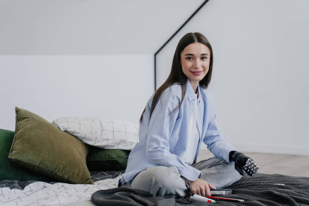 istock Smiling young woman with a bionic arm sitting on a bed, surrounded by a modern minimalist decor 1917605559