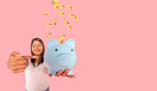 Happy woman in white shirt discovering empty piggy bank without savings. Investment, saving money, currency, deposit. Indoor studio shot isolated on pink background.