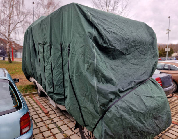 the camper van is equipped with a wheel bar behind the towing device. the parking lot is inhabited by travelers in a caravan. the cat watches over the stool like a dog, camouflage - camping mobile home vacations tent stock-fotos und bilder
