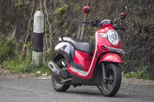 Magetan, Indonesia - August 13, 2023: A red Honda Scoopy automatic scooter parked on the side of the highway.