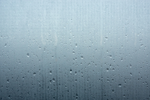 Foggy opaque glass with many small and large drops of water. The upper part is lighter than the lower part. Close-up. Background. Texture.