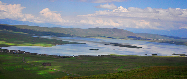 Experience the serene beauty of Aktas Lake in Ardahan, Turkiye, where lush green fields embrace the tranquil waters against a backdrop of majestic mountains. This idyllic scene of natural tranquility captures the essence of a summer's day, offering a picturesque view of pristine nature and serene landscapes.