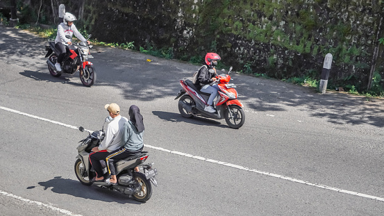 Magetan, Indonesia - August 13, 2023: Motorcycle riders on the highway who do not use or wearing helmets and violate the traffic rules. Concept for safety riding gears, careless, bad bikers.