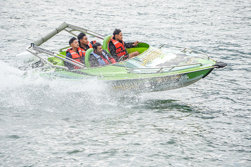Magetan, Indonesia - August 13, 2023: The Indonesian tourists ride the speedboat at high speed together with an expert guide at the tourist attraction at Telaga Sarangan Lake, East Java.