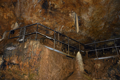 Iron stairs with railings in an underground cave. Clay stalactites hang from the ceiling and stalagmites grow from the floor. Speleological research and study of caves and the bowels of the earth