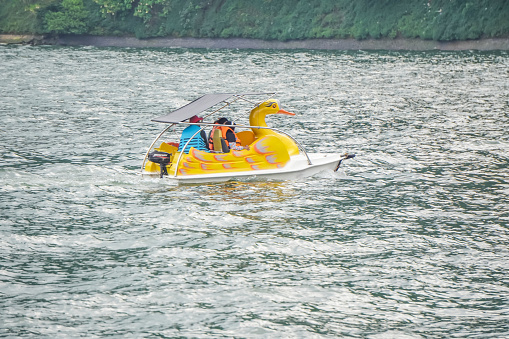 Magetan, Indonesia - August 13, 2023: The Indonesian tourists ride the duck shaped paddling boats attraction at Telaga Sarangan Lake, East Java. Concept for family vacation and leisure activity.