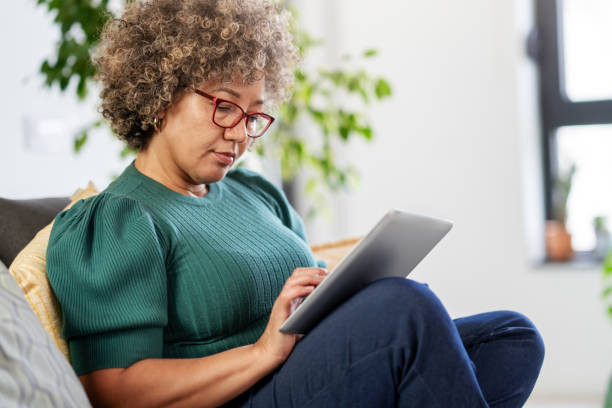 istock Beautiful middle-aged woman using a computer tablet to read a book and surf internet 1917656118