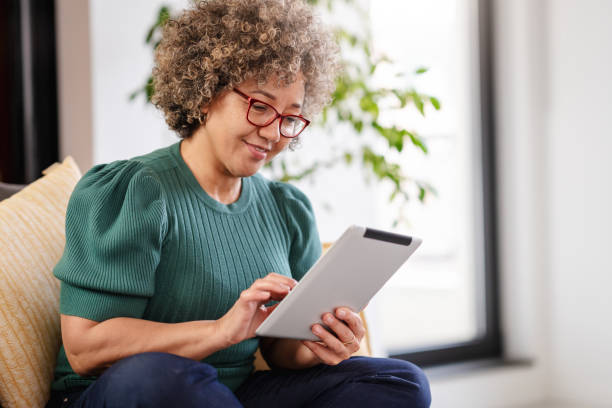 Beautiful middle-aged woman using a computer tablet to read a book and surf internet Beautiful middle-aged woman using a computer tablet to read a book and surf internet. Modern technologies used by elderly people. Mature woman using digital tablet at home old woman smiling tablet stock pictures, royalty-free photos & images