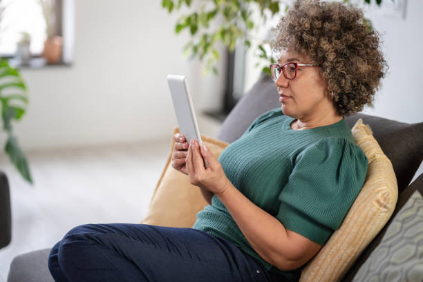 istock Beautiful middle-aged woman using a computer tablet to read a book and surf internet 1917659838