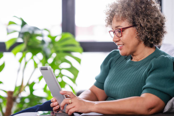 istock Beautiful middle-aged woman using a computer tablet to read a book and surf internet 1917665748