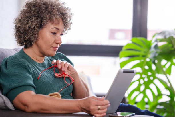 istock Beautiful middle-aged woman using a computer tablet to read a book and surf internet 1917665758