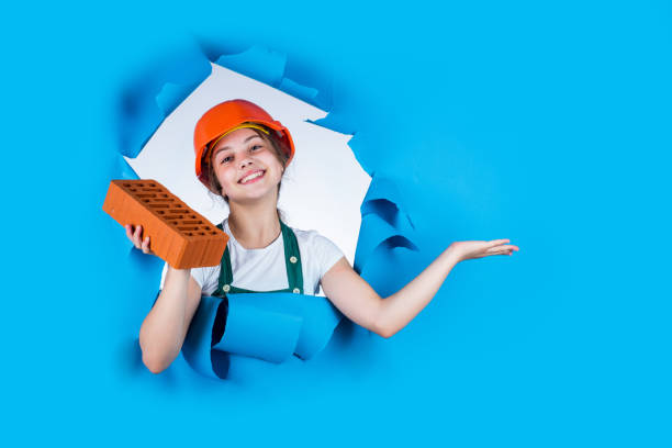 istock happy kid engineer with brick in hard hat, work tool, presenting product 1917665780