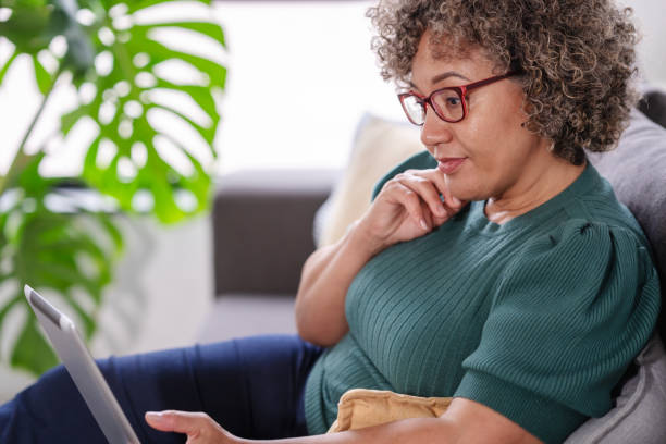 istock Beautiful middle-aged woman using a computer tablet to read a book and surf internet 1917666313