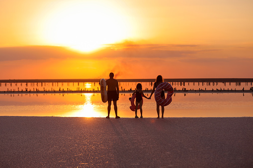 happy family walk on sunset by the sea. mom, dad and child daughter having fun on summer holiday vacation in nature. travel kid dream concept. dramatic sunset.