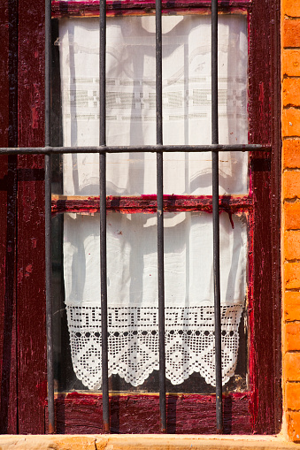 Oldrural  stone house, closed window, embroidery curtain, railing bars. Old town Castrillo de los Polvazares, León, Castilla y León, Spain.
