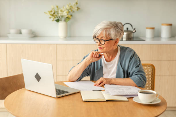 istock Online education courses webinar concept. Middle aged senior woman using laptop computer writing notes. Focused mature old woman enjoying studying online from home written records doing online work. 1917689206