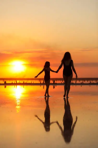 Photo of Happy family summer travel holiday. Silhouette of mom with child daughter holding hands walking together on beach on sunset. Happy mothers day. Concept of family values. International Children's Day