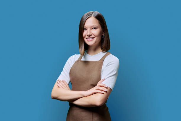 istock Young smiling woman in apron looking at camera on blue studio background 1917725843