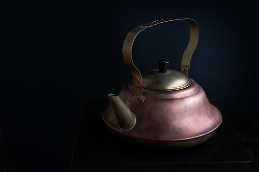 old, brass and copper kettle on wooden cabinet and black background