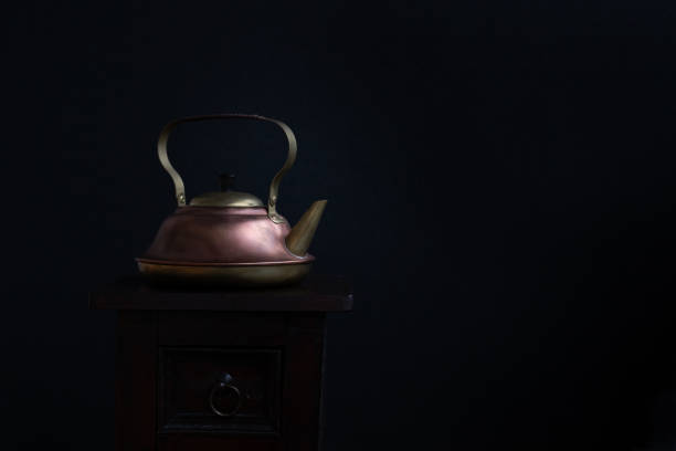 old, brass and copper kettle on wooden cabinet and black background