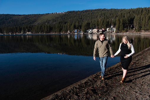 Pregnant couple go for a walk around a beautiful mountain lake in California