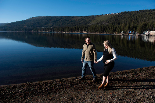 Pregnant couple go for a walk around a beautiful mountain lake in California