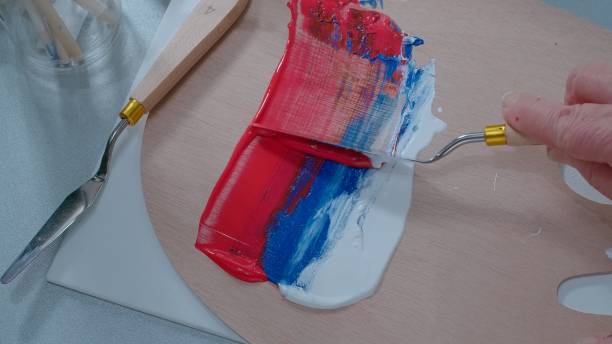 Close-Up Shot of an Artist Mixing Together White, Blue and red oil paints with a Palette Knife stock photo