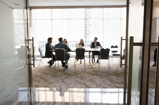 Group of businesspeople sitting at large conference table in negotiation room. Project partners brainstorming on ideas, discussing collaboration terms, teamwork. Business meeting blurred background