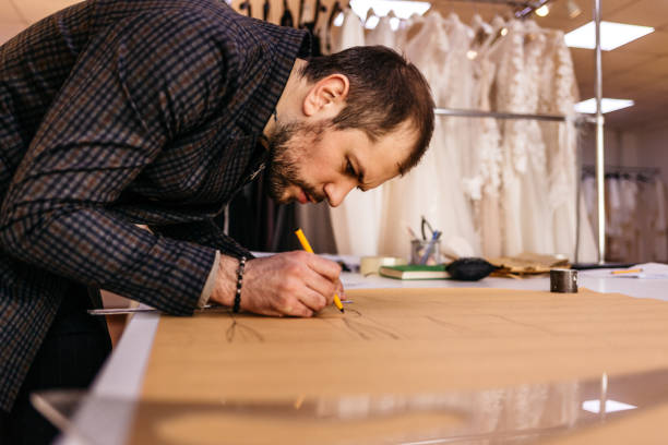 istock Young serious tailor with beard looking at drawing near wooden table with threads in amazing atelier with antique furniture and mannequin 1917756864