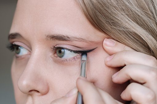 Cropped shot of a young caucasian blonde woman using a contour brush while drawing arrows on the eyelids. A girl applying a makeup. Close up