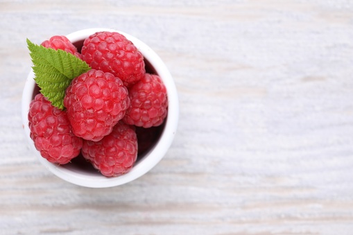 Tasty ripe raspberries and green leaf on white wooden table, top view. Space for text