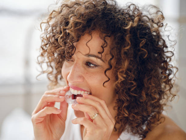 Woman in Bed in the Morning Using Clear Teeth Aligners 스톡 사진