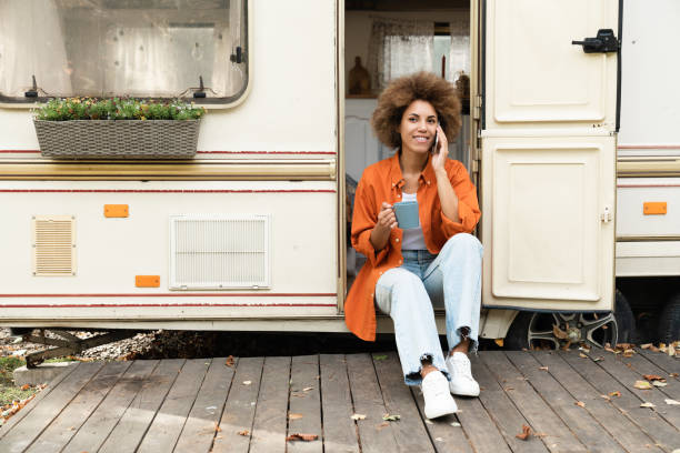 remote-jobarbeit, freiberuflich. junge afrikanische frau alleinreisende, die mit kunden, partnern, freunden telefoniert, während sie auf einem van mit wohnmobil auf rädern unterwegs ist - motor home mobile home isolated vehicle trailer stock-fotos und bilder