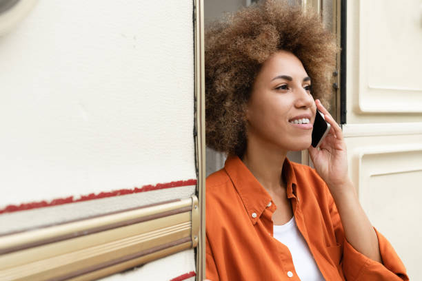 podróż w pojedynkę, samotnie w przygodzie. szczęśliwy afrykański młody podróżnik kobieta freelancer rozmawia przez telefon smartfon z klientami krewnymi przyjaciółmi, relaksujące podróżowanie w przyczepie van przyczepa samochód kempingowy, d - motor home mobile home isolated vehicle trailer zdjęcia i obrazy z banku zdjęć