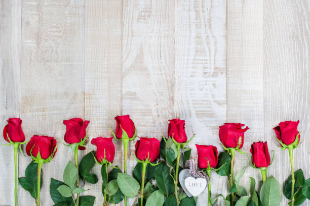 праздничный фон из светлой деревянной поверхности с рамкой из красных роз и деревянных сердечек на рустикальной ленте.стильный цветочный � - wedding reception valentines day gift heart shape стоковые фото и изображения