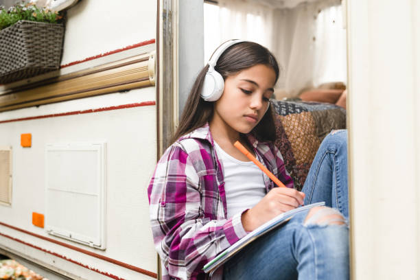 pequeña niña preadolescente niña hija niño niño escuchando la música, dibujando, haciendo la tarea mientras viaja en remolque, autocaravana, furgoneta, remolque, remolque de autocaravana, remolque - mobile home audio fotografías e imágenes de stock