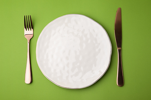 Clean plate with cutlery on green background, flat lay