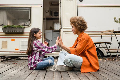 Mixed-race daughter and african mother playing games together, clapping hands, spending time on a road trip while traveling by van motor home trailer