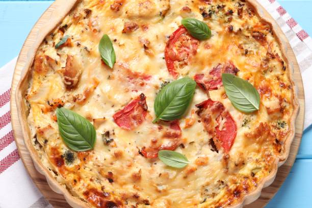 istock Tasty quiche with tomatoes, basil and cheese served on light blue wooden table, top view 1917914935