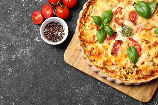 Tasty quiche with tomatoes, basil and cheese served on dark textured table, flat lay. Space for text