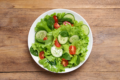 Delicious salad in bowl on wooden table, top view