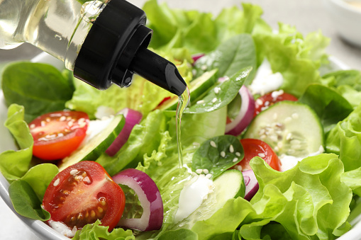 Pouring oil into delicious salad in bowl, closeup