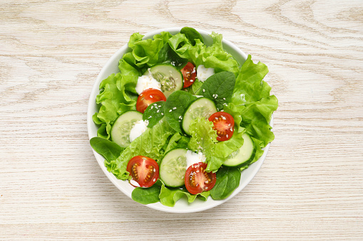 Delicious salad in bowl on white wooden table, top view