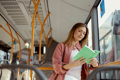 Young woman reading book in the modern tram, happy passenger moving by comfortable public transport