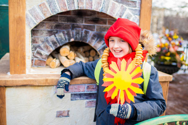 bambino felice al tradizionale festival russo maslenitsa, settimana delle frittelle. il ragazzo tiene in mano il sole, simbolo dell'arrivo della primavera, sta accanto alla stufa alla fiera. - russian culture russia child people foto e immagini stock