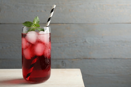 Glass of delicious iced hibiscus tea with mint and straw on wooden table, space for text
